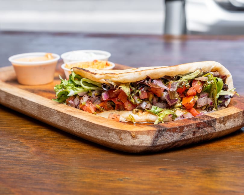 A pita bread sandwich filled with lettuce, tomatoes, and onions, served with two dipping sauces.