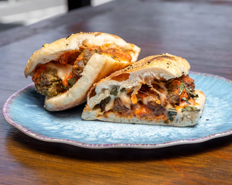 Two halves of a meatball sub sandwich with melted cheese and sauce on a blue plate.