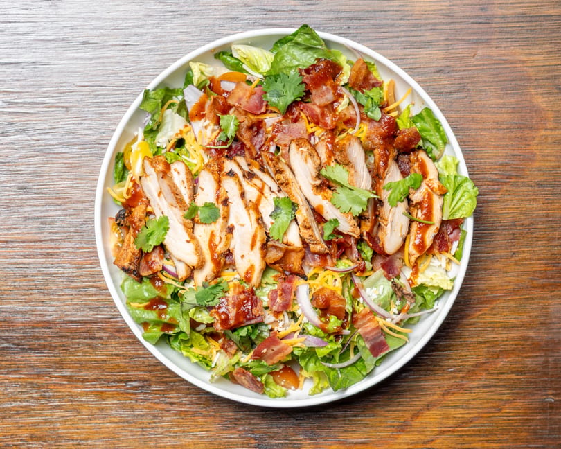 Overhead view of a BBQ chicken salad with bacon, cheese, red onion, and cilantro.