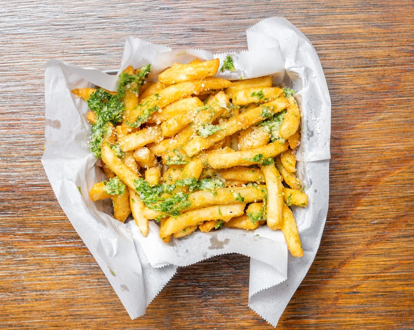 Golden french fries topped with green herbs and grated cheese, served in a paper-lined basket.
